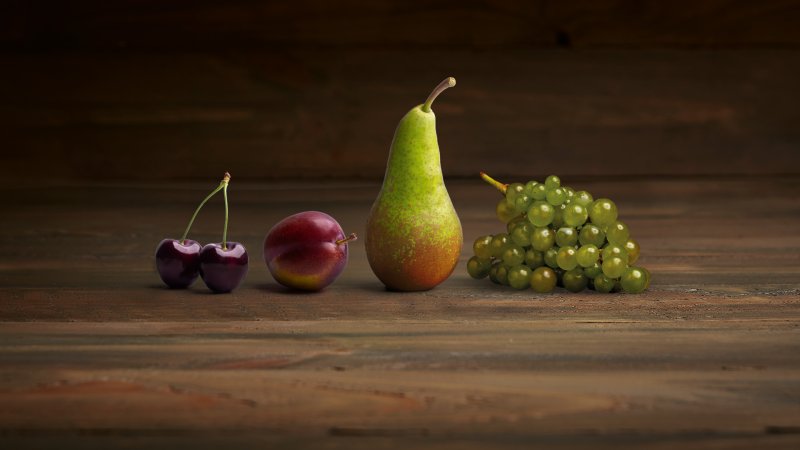vier fruitsoorten op een rij: kers, pruim, peer en druif, met een houten achtergrond
